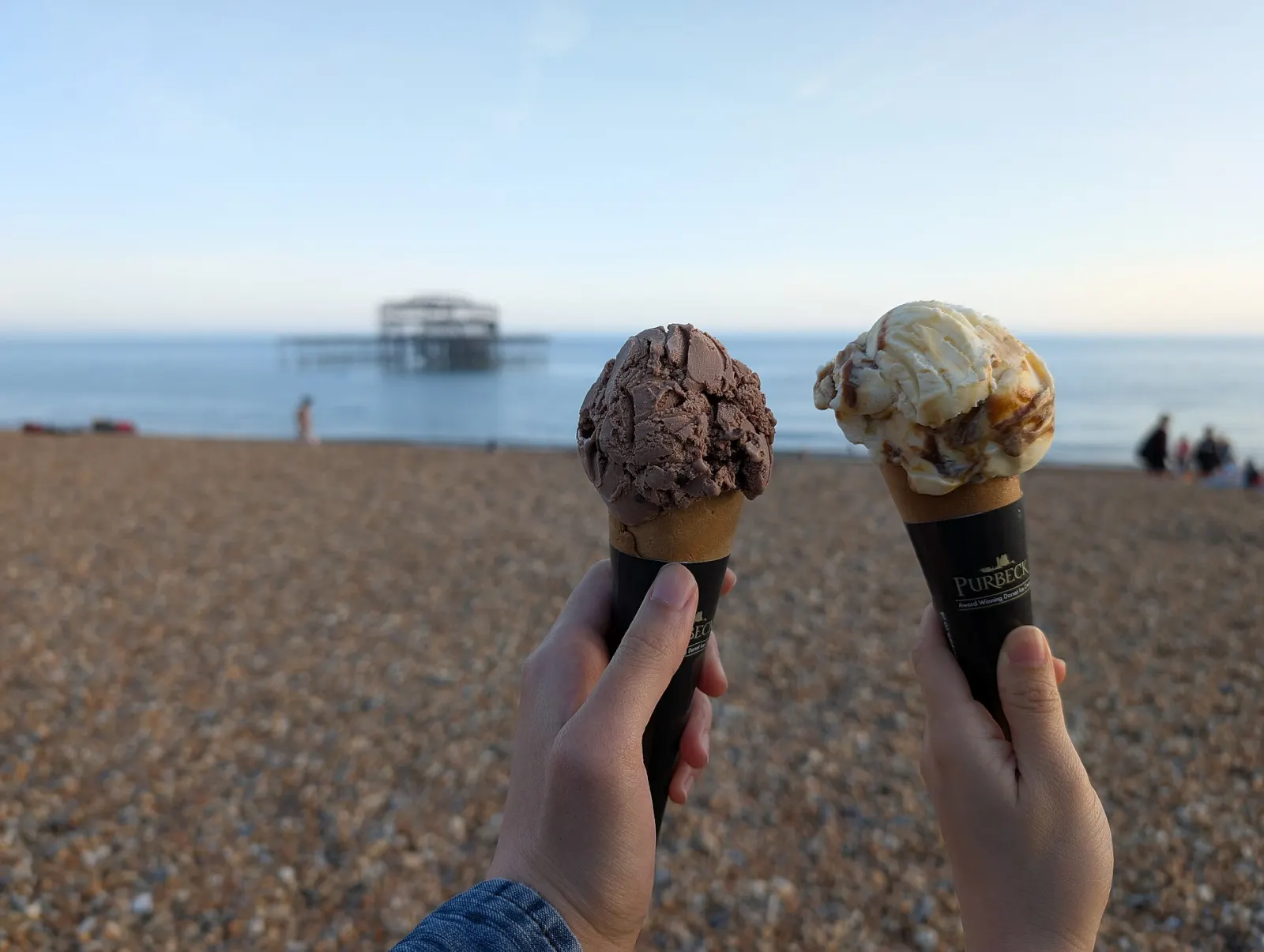 Two scoops of ice cream in cones held up on a beach. The photo was not taken in Wesley Chapel.