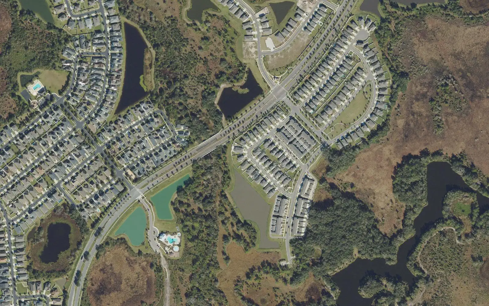 Homes along curving streets, a community pool and stormwater ponds beside wetlands in Avalon Park West, seen from above.