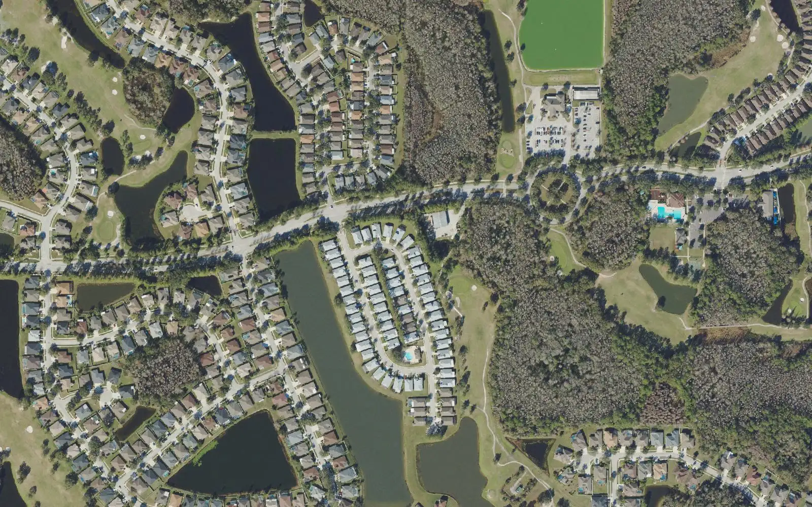 Homes and lakes along a curving boulevard in Lexington Oaks, with golf course fairways at left and right, seen from above.