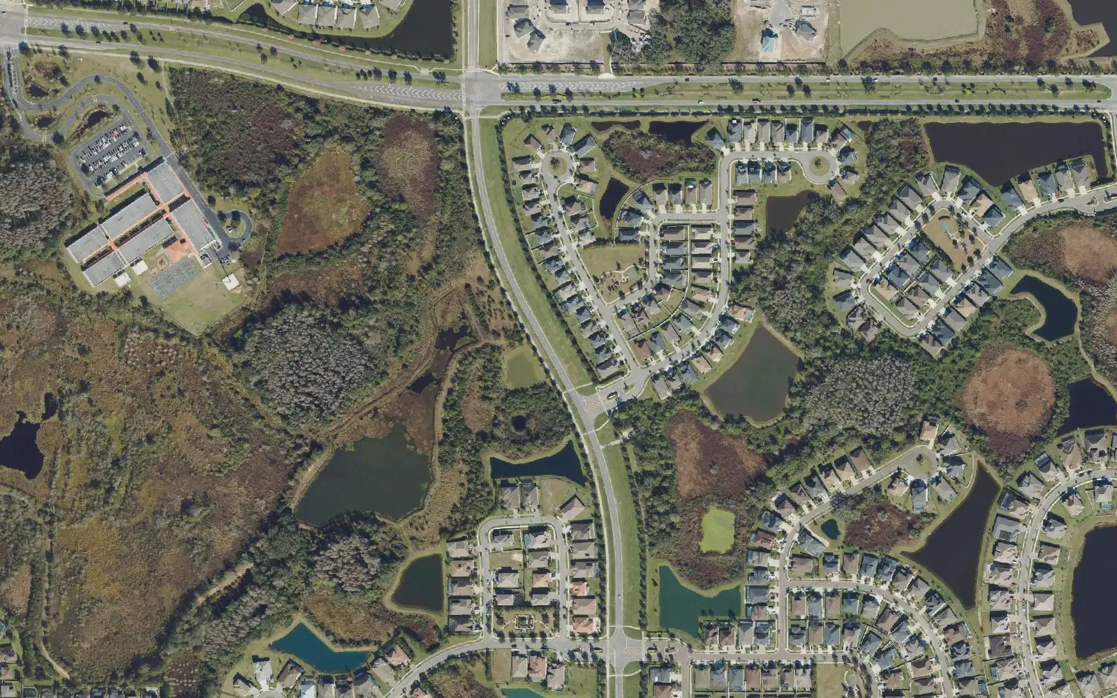 Watergrass Elementary School at left and streets of homes around ponds, with a main road curving through, in an aerial view of Watergrass.